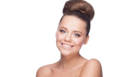 Young beautiful smiling girl with hair bun and makeup looking at camera, over white background