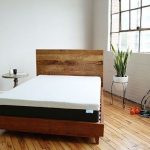 BEar mattress in a well lit room with a wooden bedframe and a plant in the corner