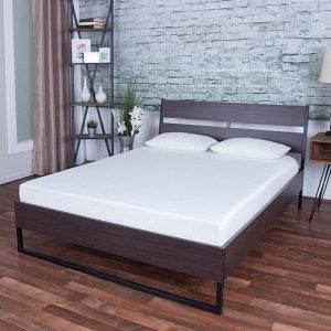 Image of a soft reflex foam based bed in a show-room with a wood bed-frame and gray brick wall behind it