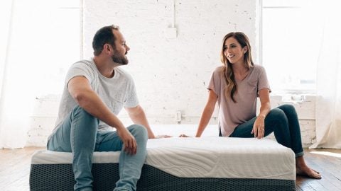 A man and woman sitting on a Voila mattress speaking to each other and testing the edge support