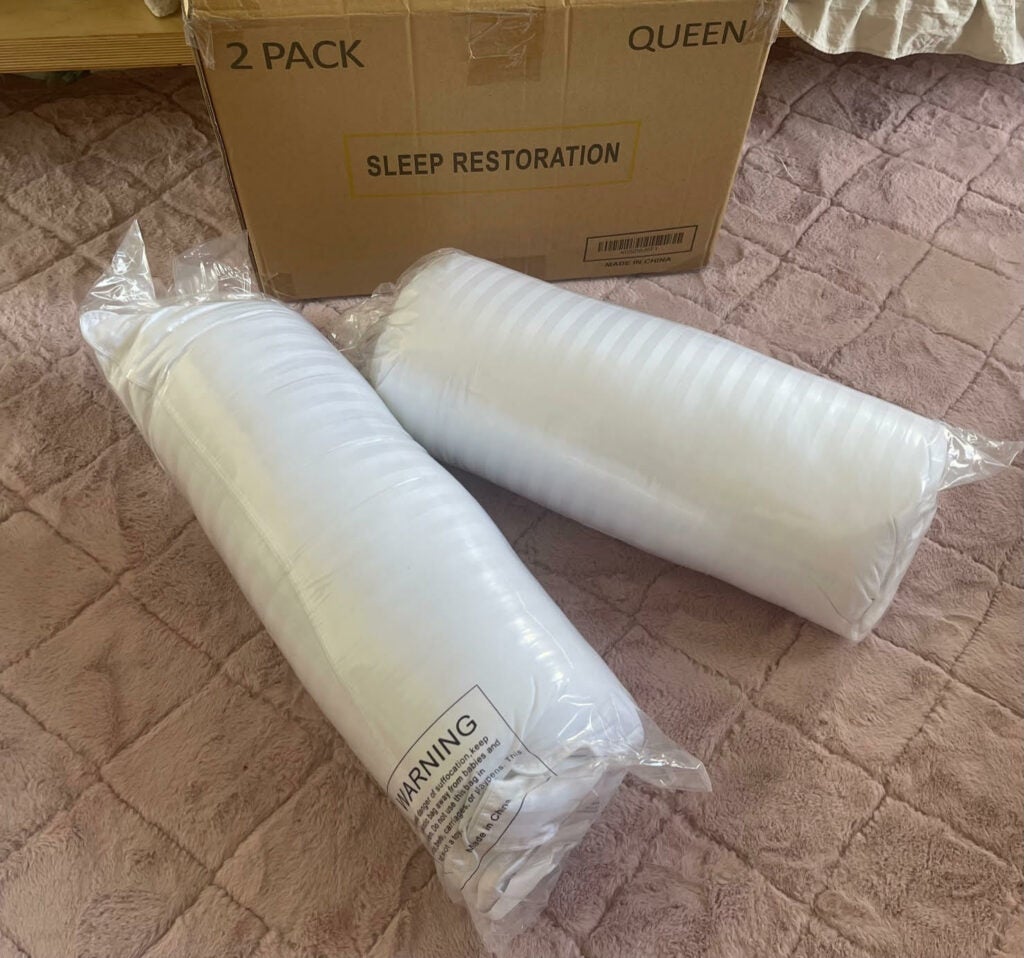 Sleep Restoration two pillows rolled up in packaging, beside brown box