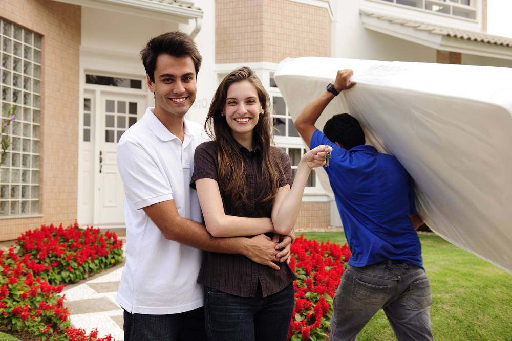 couple posing for photo while another guy carries mattress