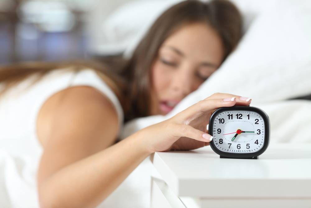 female turning off traditional alarm clock